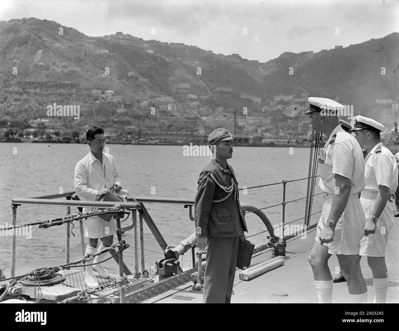 HONGKONG WIEDER BESETZT. 30. AUGUST 1945, HONGKONG, VOR, WÄHREND UND NACH DER WIEDERBESETZUNG DER KRONENKOLONIE. - Ein japanischer Gesandter und sein Dolmetscher kommen an Bord der HMS SWIFTSURE, die vorübergehend die Flagge von Konteradmiral C H J Harcourt tragen, unmittelbar nach der Besetzung Hongkongs durch die Task Force unter seinem Kommando. Der Gesandte wurde von Captain P V MacLaughlin im Kommando der HMS SWIFTSURE verhört und wird von Lieutenant G Albert aus Südafrika auf dem Weg zum Quarterdeck getroffen Stockfoto