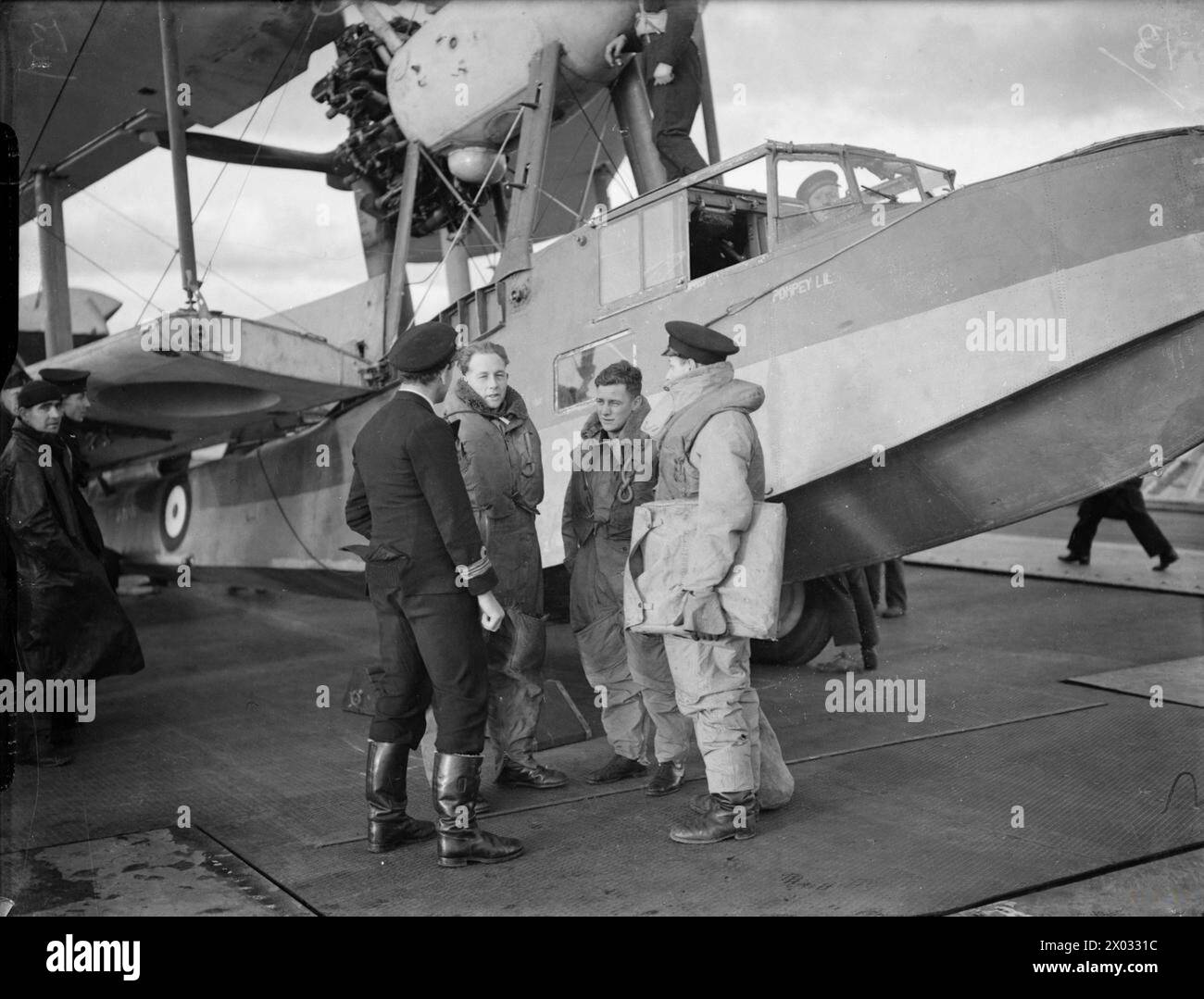 DIE ROYAL NAVY WÄHREND DES ZWEITEN WELTKRIEGS - die Besatzung, der Pilot, der Beobachter und der Luftschütze, berichten dem Commanding Officer über den Ausstieg aus ihrem Supermarine Walrus Flugzeug an Bord des Flugzeugträgers HMS ARGUS. Beachten Sie das Mitglied der Schiffsbesatzung im Cockpit Royal Navy, HMS Argus, Aircraft Carrier, (1917) Stockfoto