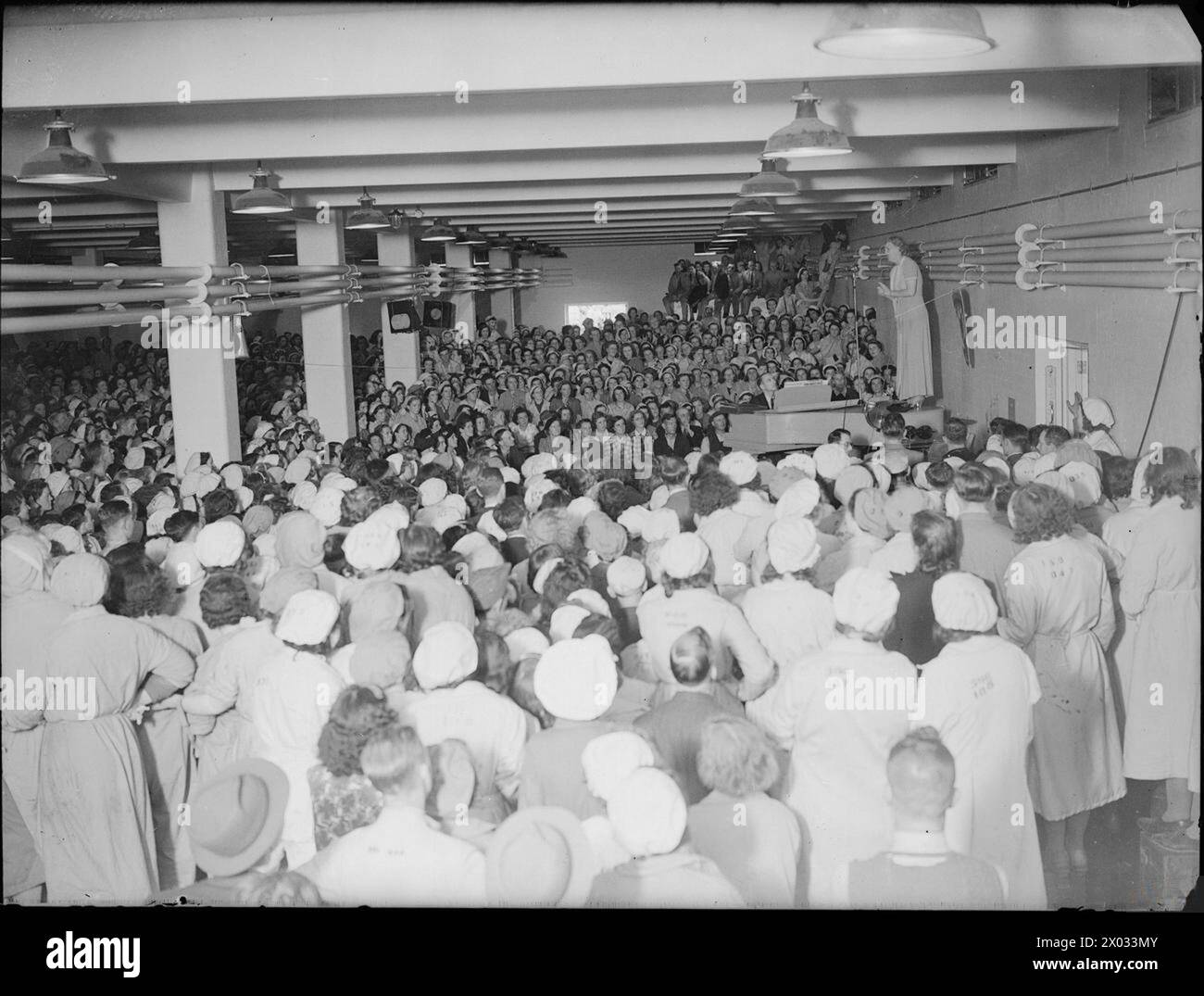 Sängerin Gracie Fields tritt 1941 auf einem Flügel für eine große Menge von Munitionsarbeitern in einer britischen Kampfmittelfabrik auf, möglicherweise ROF Kirkby in Liverpool. Stockfoto Sängerin Gracie Fields tritt 1941 auf einem Flügel für eine große Menge von Munitionsarbeitern in einer britischen Kampfmittelfabrik auf, möglicherweise ROF Kirkby in Liverpool. Stockfoto
