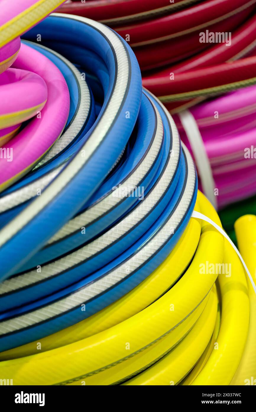 Zusammengerollter bunter Gartenschlauch, blau, gelb, rot und rosa, Nahaufnahme, selektiver Fokus, abstrakter Gartenhintergrund Stockfoto