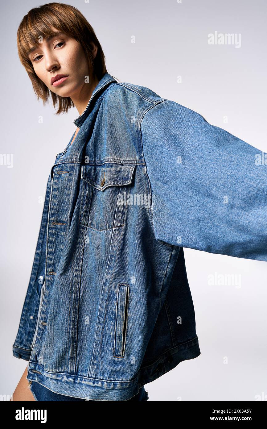 Eine junge Frau mit kurzen Haaren posiert selbstbewusst für ein Foto in einem Studio und trägt eine trendige jeansjacke. Stockfoto
