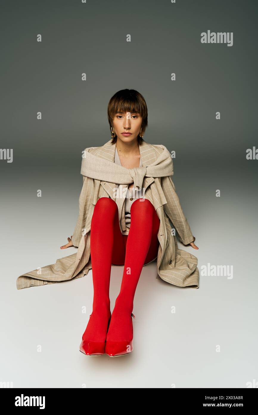 Eine junge Frau mit kurzen Haaren sitzt elegant auf dem Boden und trägt auffällige rote Strümpfe in einem Studio. Stockfoto