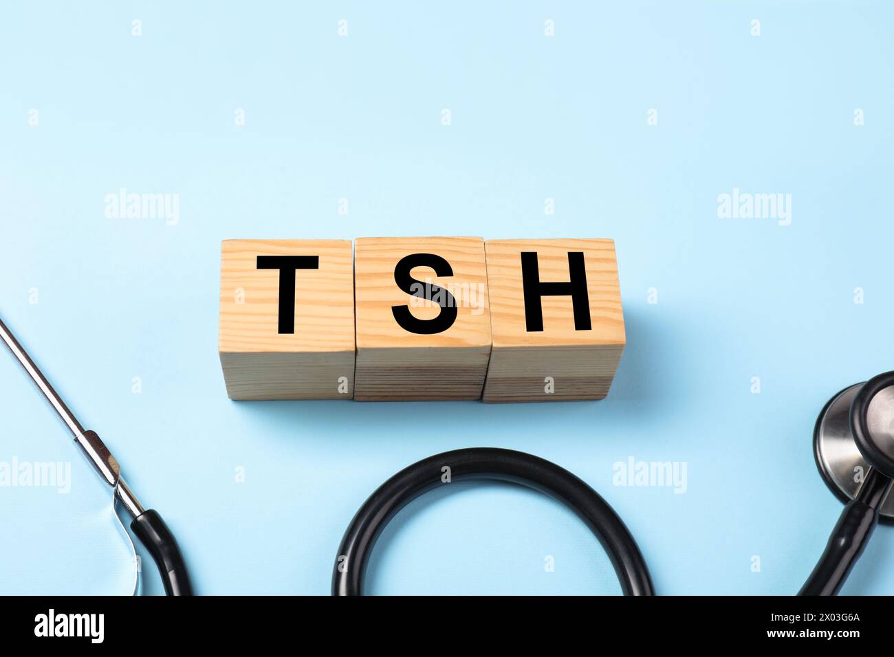 Endokrinologie. Stethoskop und Holzwürfel mit Schilddrüsenhormonen auf hellblauem Hintergrund. Leerzeichen für Text Stockfoto