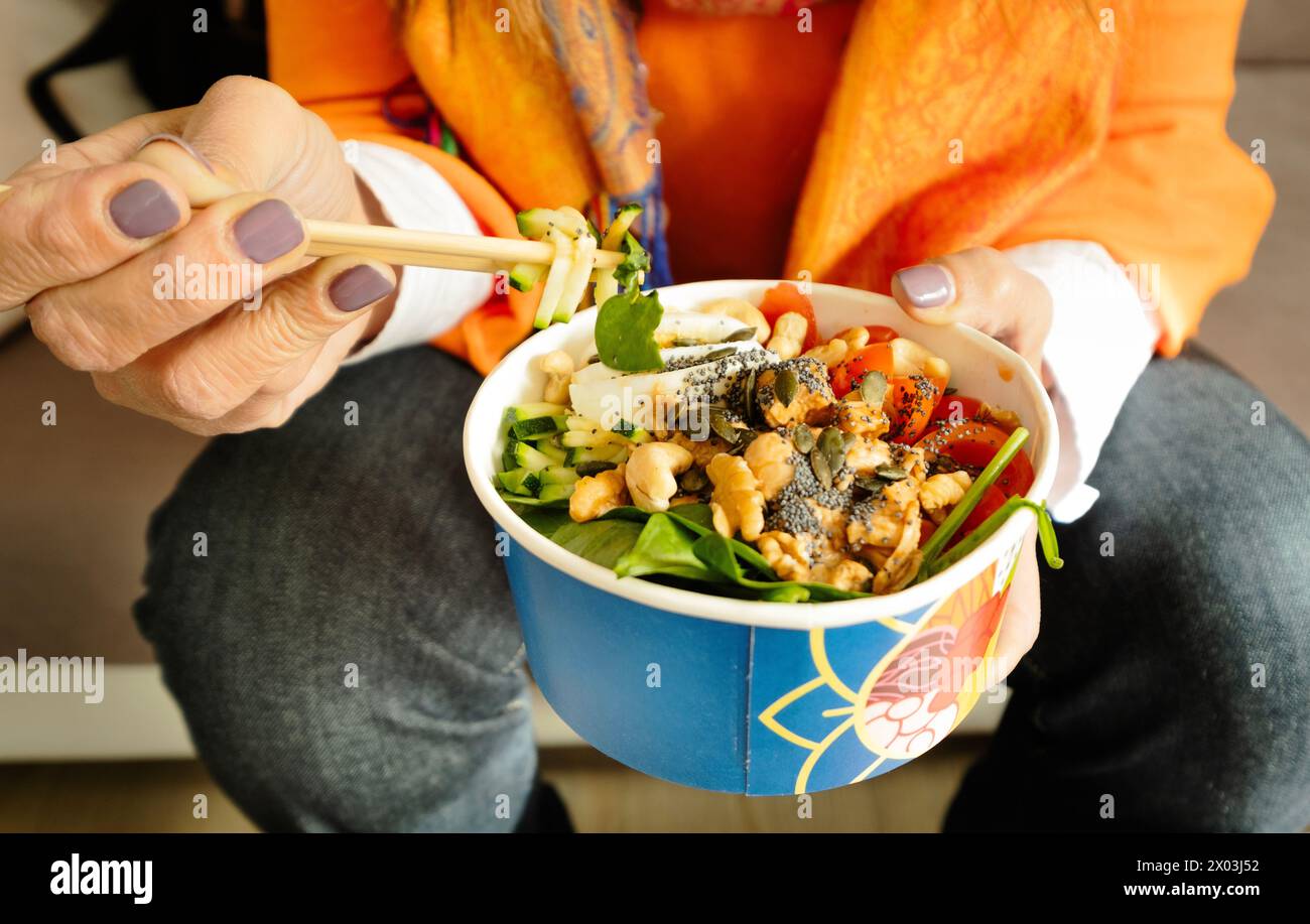 Nahaufnahme einer Frauenhand, die eine bunte Schüssel asiatischen Salats (Poke) mit Stäbchen hält Stockfoto