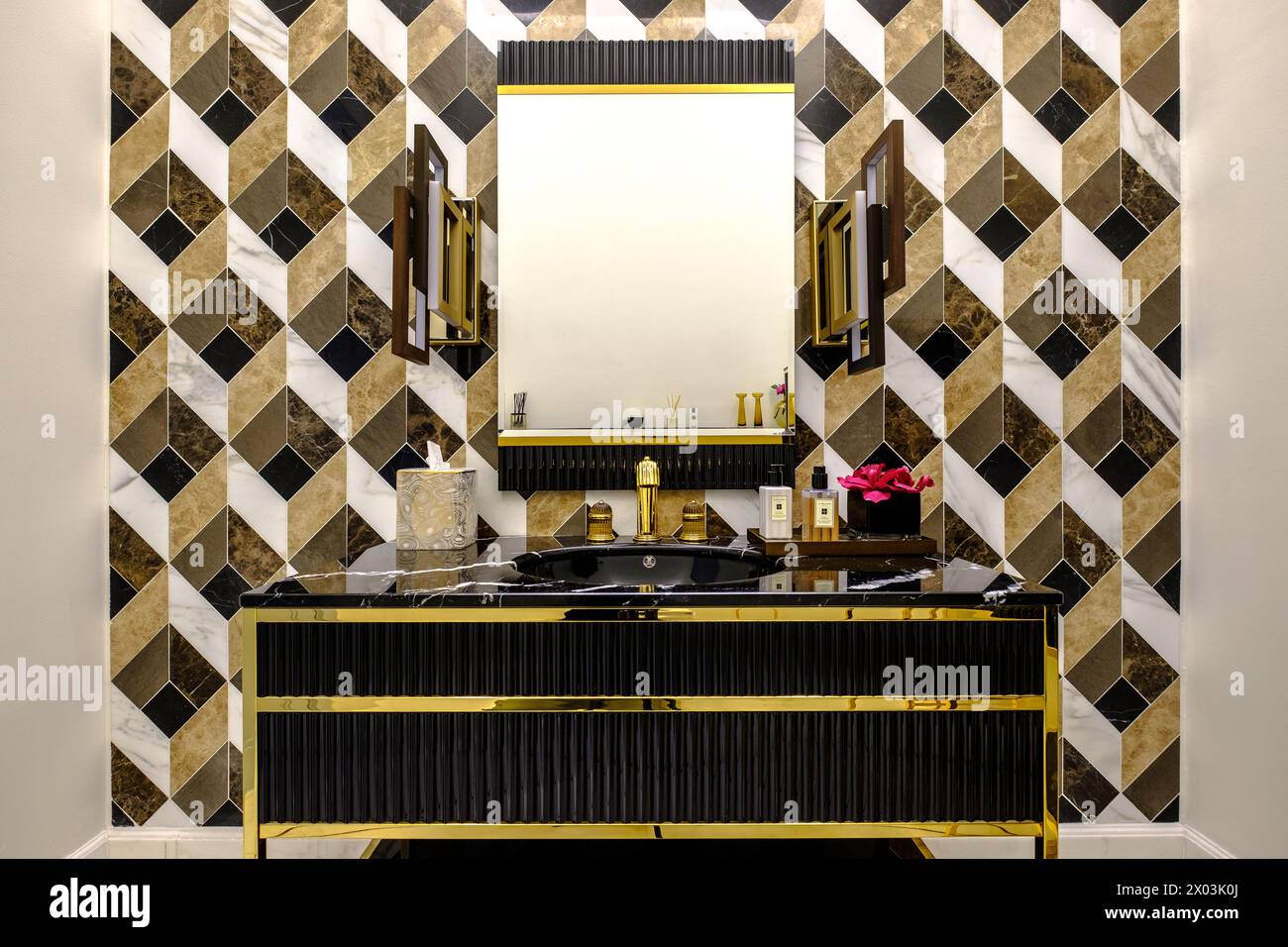 HAMALA, BAHRAIN - 2. MÄRZ 2019: Elegantes, modernistisches Waschbecken aus schwarzem Marmor mit Spiegel und Goldbeschlägen und einer gefliesten Wand im Badezimmer einer Luxusvilla. Stockfoto