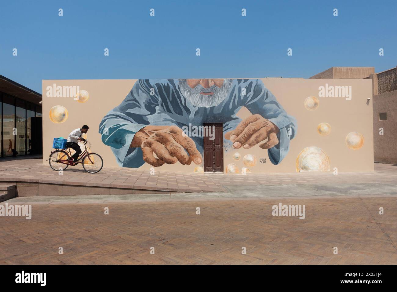 Radfahrer fahren vorbei an einem riesigen Wandgemälde im Al Shindagha Historical District, Dubai, Vereinigte Arabische Emirate. Stockfoto
