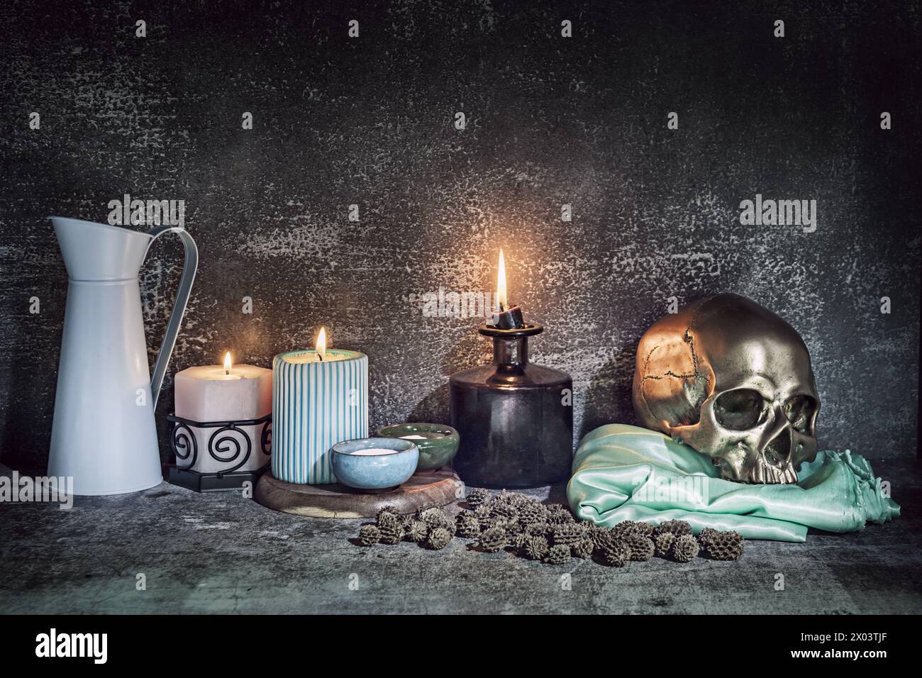 Ein Stillleben mit einem goldenen Schädel auf einem grünen Satintuch neben mehreren zündeten Kerzen Stockfoto