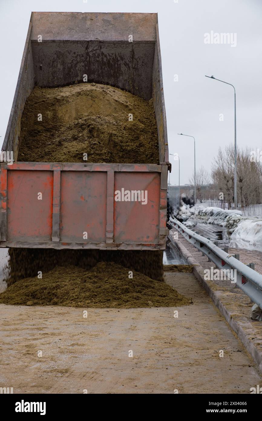 Der Kipplader entlädt Sand, um die Beutel zu befüllen, die vor Überflutung geschützt sind Stockfoto