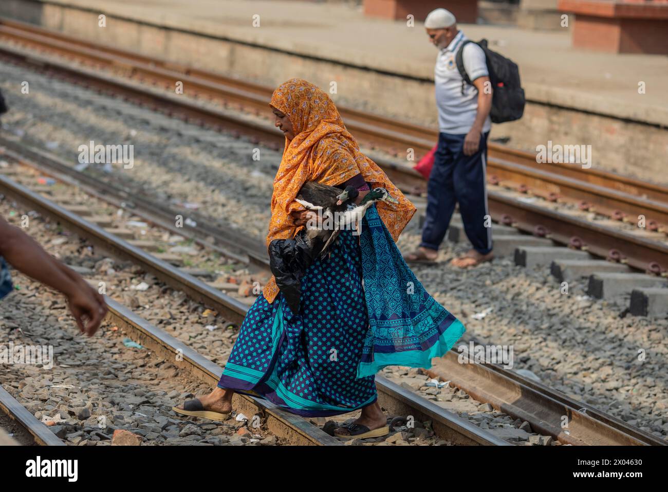 Dhaka, Bangladesch. April 2024. Eine Frau überquert die Gleise mit ihrer Ente, während sie auf die Fahrt am Bahnhof Tongi wartet. Die Menschen reisen nach Hause, um das Eid al-Fitr-Festival zu feiern, das das Ende des Heiligen Fastenmonats des Islam im Ramadan markiert. Quelle: SOPA Images Limited/Alamy Live News Stockfoto