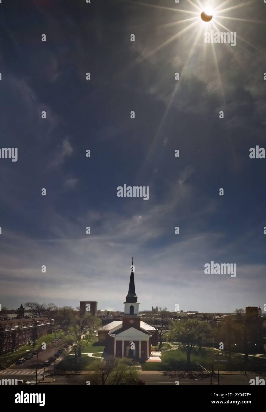 Blick auf die Stadt im Mittleren Westen im Frühling während teilweiser Sonnenfinsternis, wobei der Mond einen großen Teil der hellen Nachmittagssonne bedeckt; Straße und Gebäude im Vordergrund Stockfoto