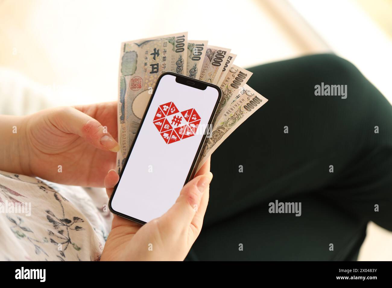 KIEW, UKRAINE - 1. APRIL 2024 Pinduoduo-Symbol auf dem Smartphone-Bildschirm und Geld in weiblicher Hand. IPhone-Display mit App-Logo und japanischen Yen-Geldscheine in Frauenhänden aus nächster Nähe Stockfoto