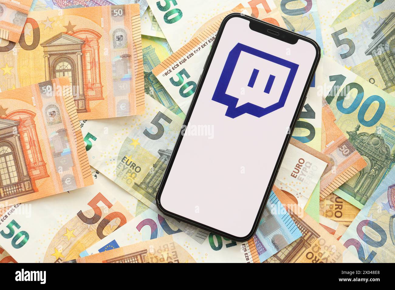 KIEW, UKRAINE - 1. APRIL 2024 Twitch das Symbol auf dem Smartphone-Bildschirm auf vielen Euro-Geldscheinen. IPhone-Display mit App-Logo mit Euro-Banknoten in europäischer Währung Stockfoto