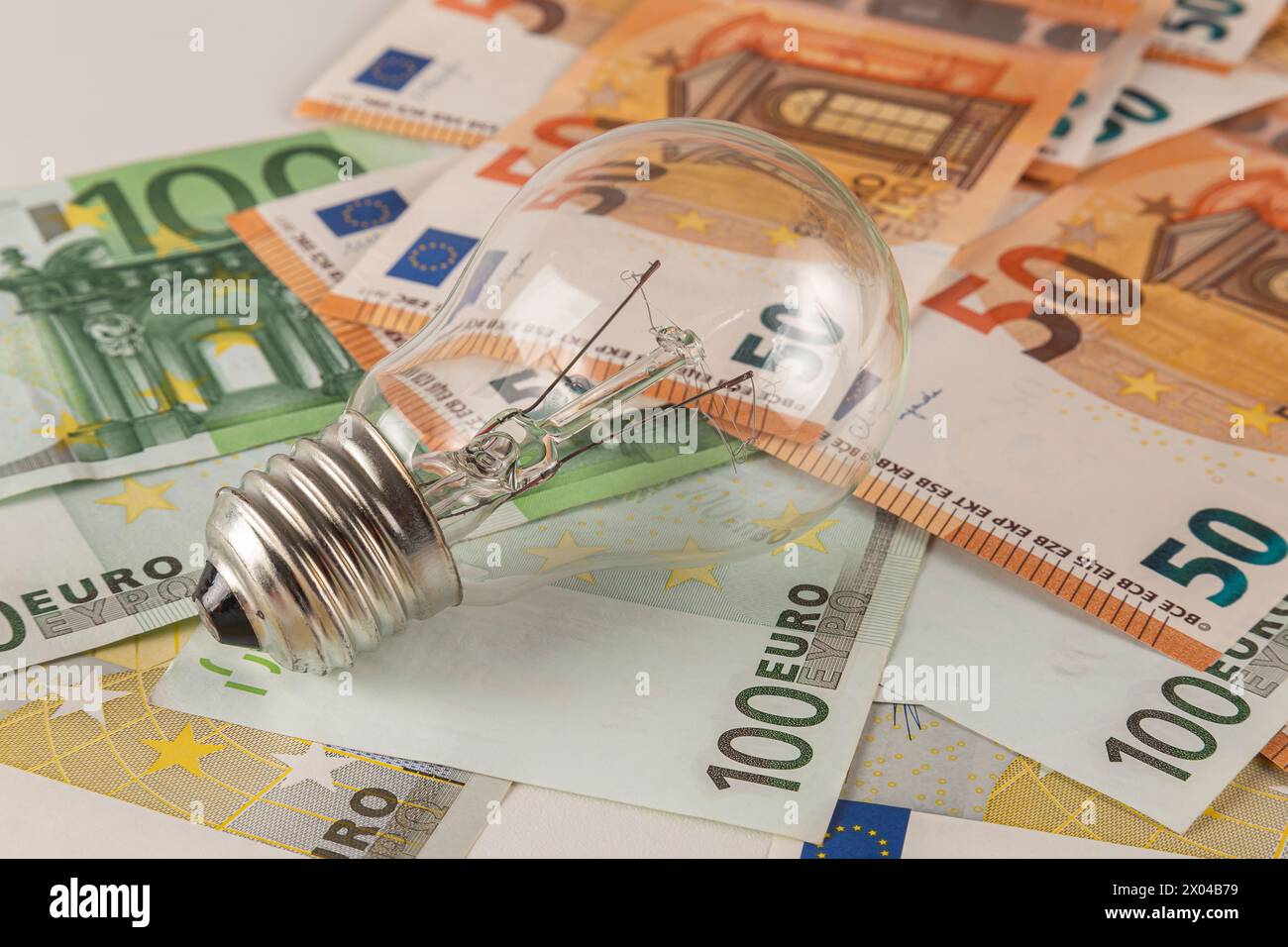 Eine Glühbirne liegt auf einem Tisch, der mit Euro-Banknoten bedeckt ist, auf einem hellen Hintergrund in Nahaufnahme Stockfoto