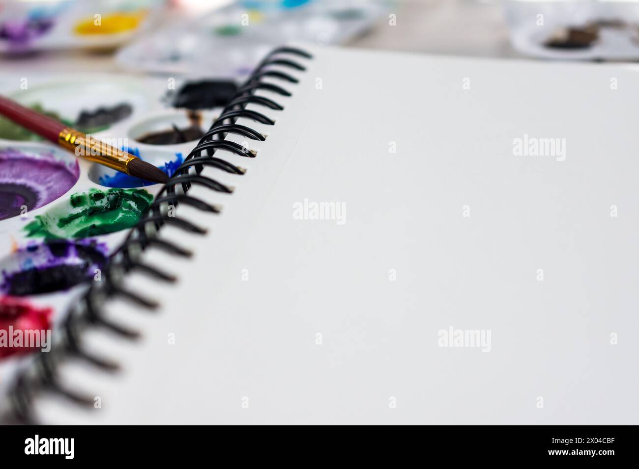 Nahaufnahme eines spiralgebundenen Notizbuchs aus Aquarellpapier. Aquarellfarben zeichnen im Hintergrund verschwommene Farben. Stockfoto