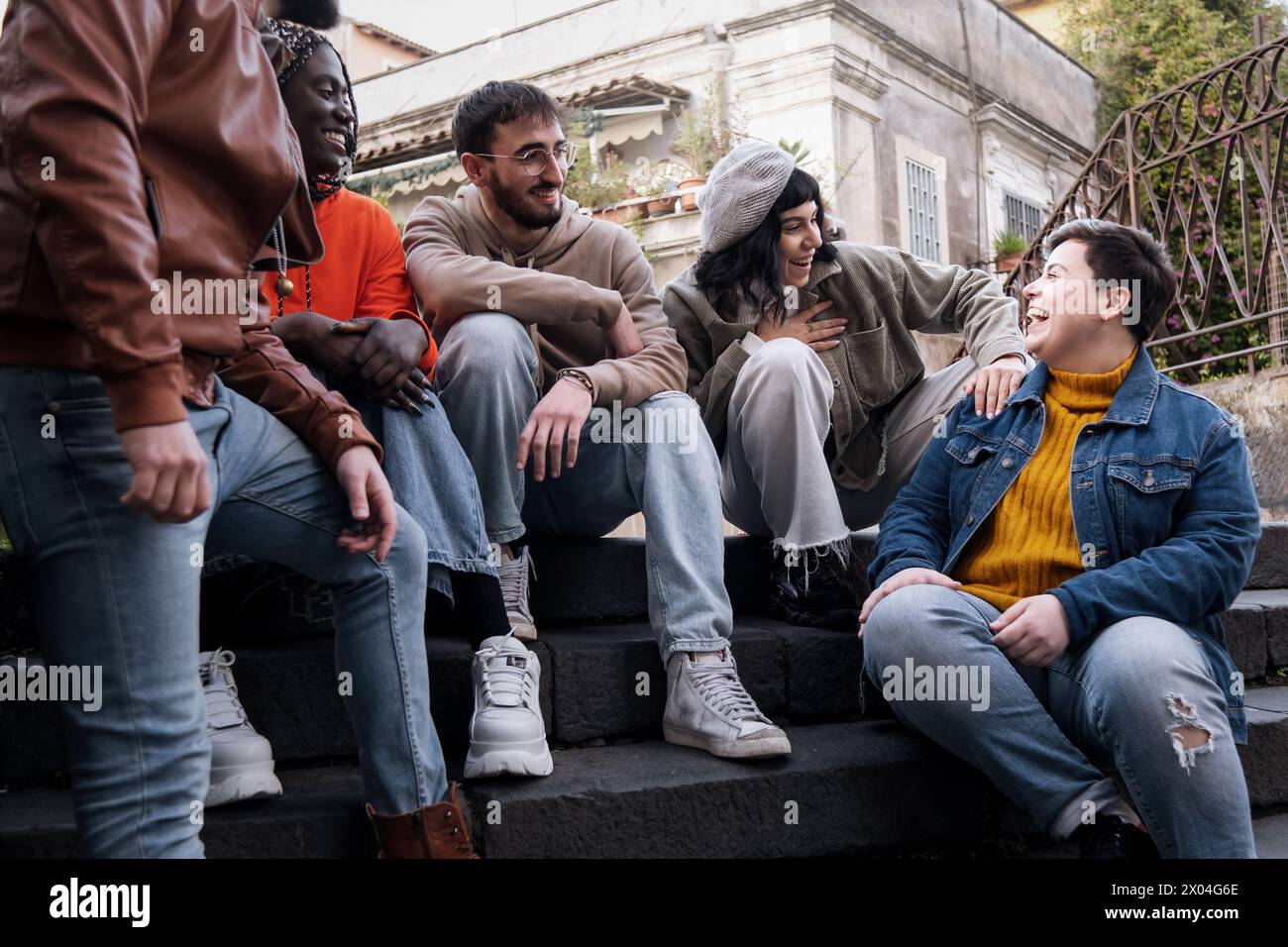 Eine Gruppe multikultureller Freunde, die auf den Stufen der Stadt lachen und Freude teilen - Junge Erwachsene zeigen den Geist der städtischen Jugend und die vielfältige Freundlichkeit Stockfoto