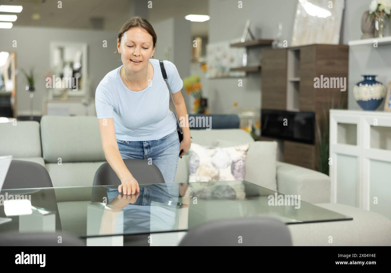 Zufriedene Frau wählt einen neuen, modernen Tisch im Möbelgeschäft Stockfoto