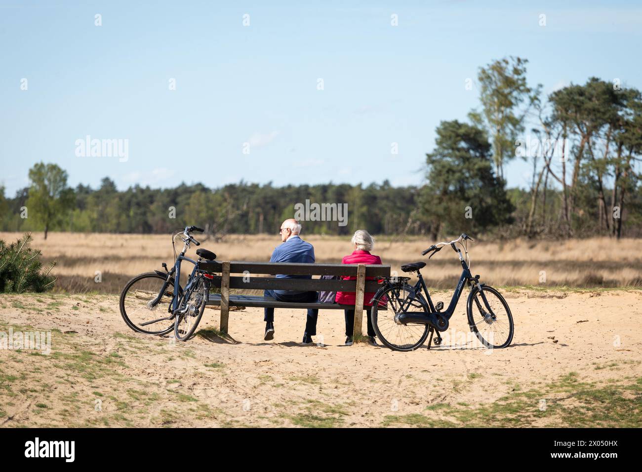 Pensioniertes Paar mit Fahrrädern, die auf einer Bank im Naturschutzgebiet Strabrechtse Heide in den Niederlanden ruhen Stockfoto