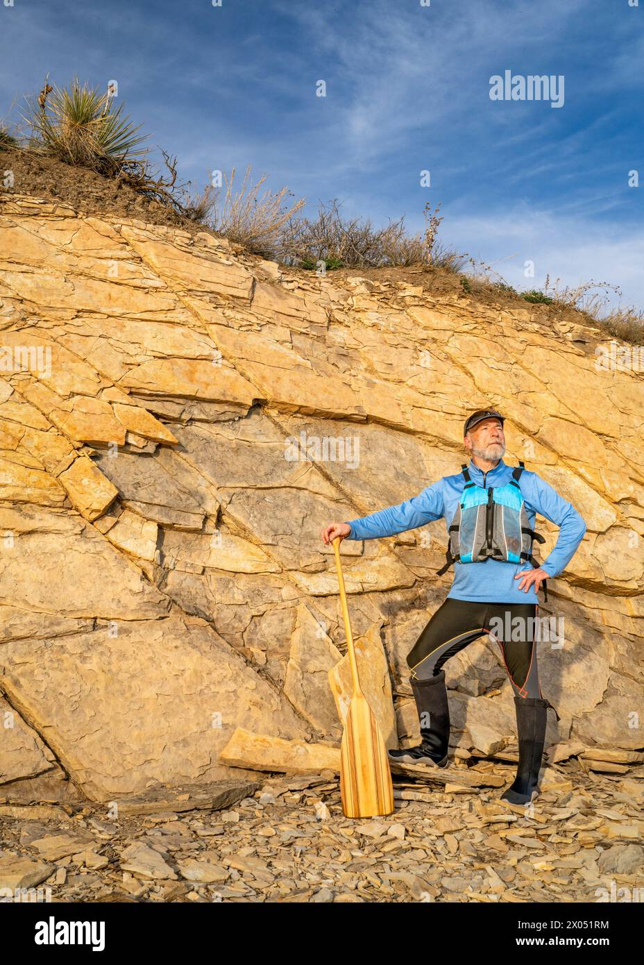 Älterer männlicher Paddler mit Schwimmweste und einem hölzernen Kanu-Paddel an einem felsigen Seeufer Stockfoto