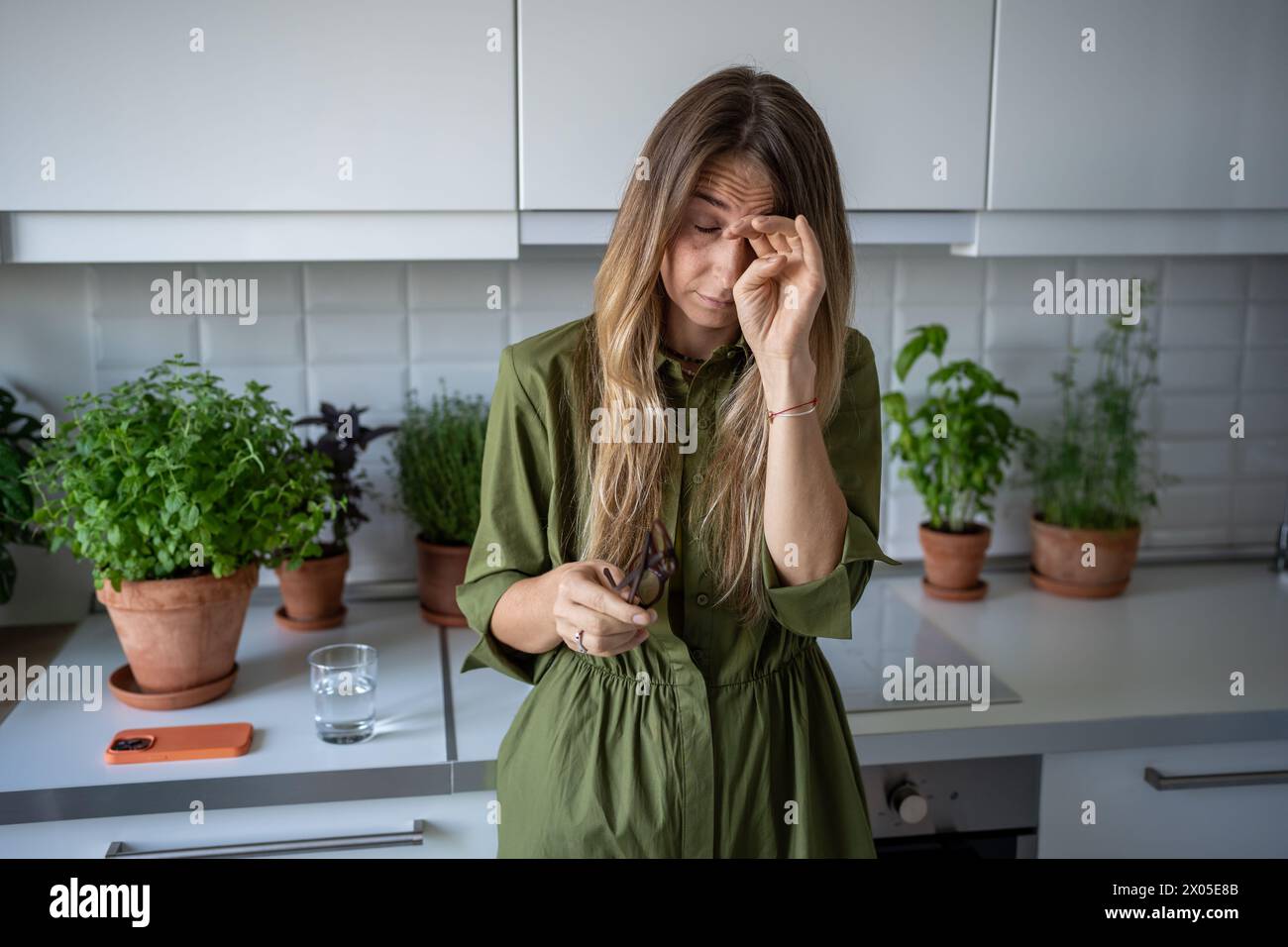 Schläfrige müde Frau, die an Schlaflosigkeit leidet, reibt am frühen Morgen die Augen auf die Küche mit Zimmerpflanzen. Stockfoto