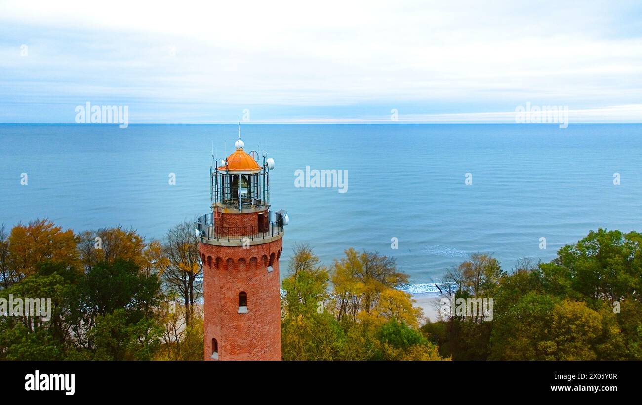 Drohnenaufnahme des Leuchtturms von Gąski, Polen, an einem bewölkten Novembertag. Das ruhige Meer, die sanften Wellen und der leere Strand schaffen eine ruhige Küstenlandschaft Stockfoto