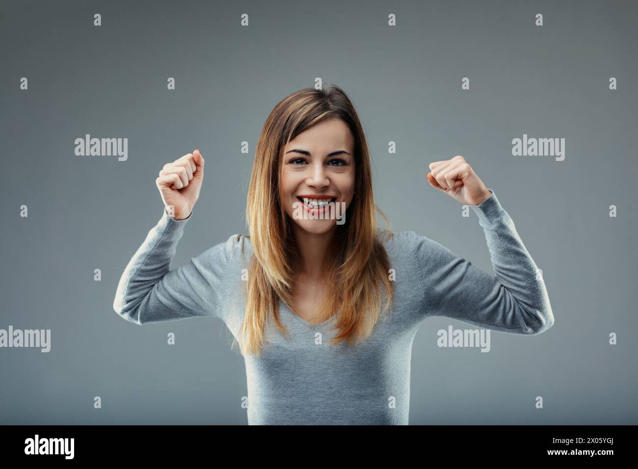 Fröhlicher Ausdruck gepaart mit der Pose eines siegers definiert den jubelnden Zustand der Dame in Grau Stockfoto