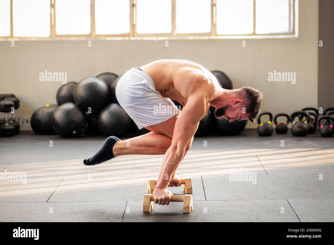 Seitenansicht eines starken muskulösen Mannes, der Tuck-Planche-Calisthenics-Übungen auf dem Boden im Fitnessstudio mit hölzernen paralletten macht Stockfoto