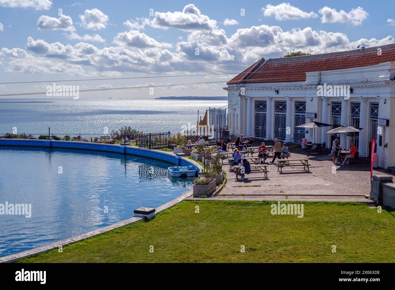 Mehrere Tische mit Leuten, die im Freien neben dem Bootspool Royal Esplanade, Ramsgate essen. Café-Gebäude auf der rechten Seite. Pedalo angedockt. Stockfoto