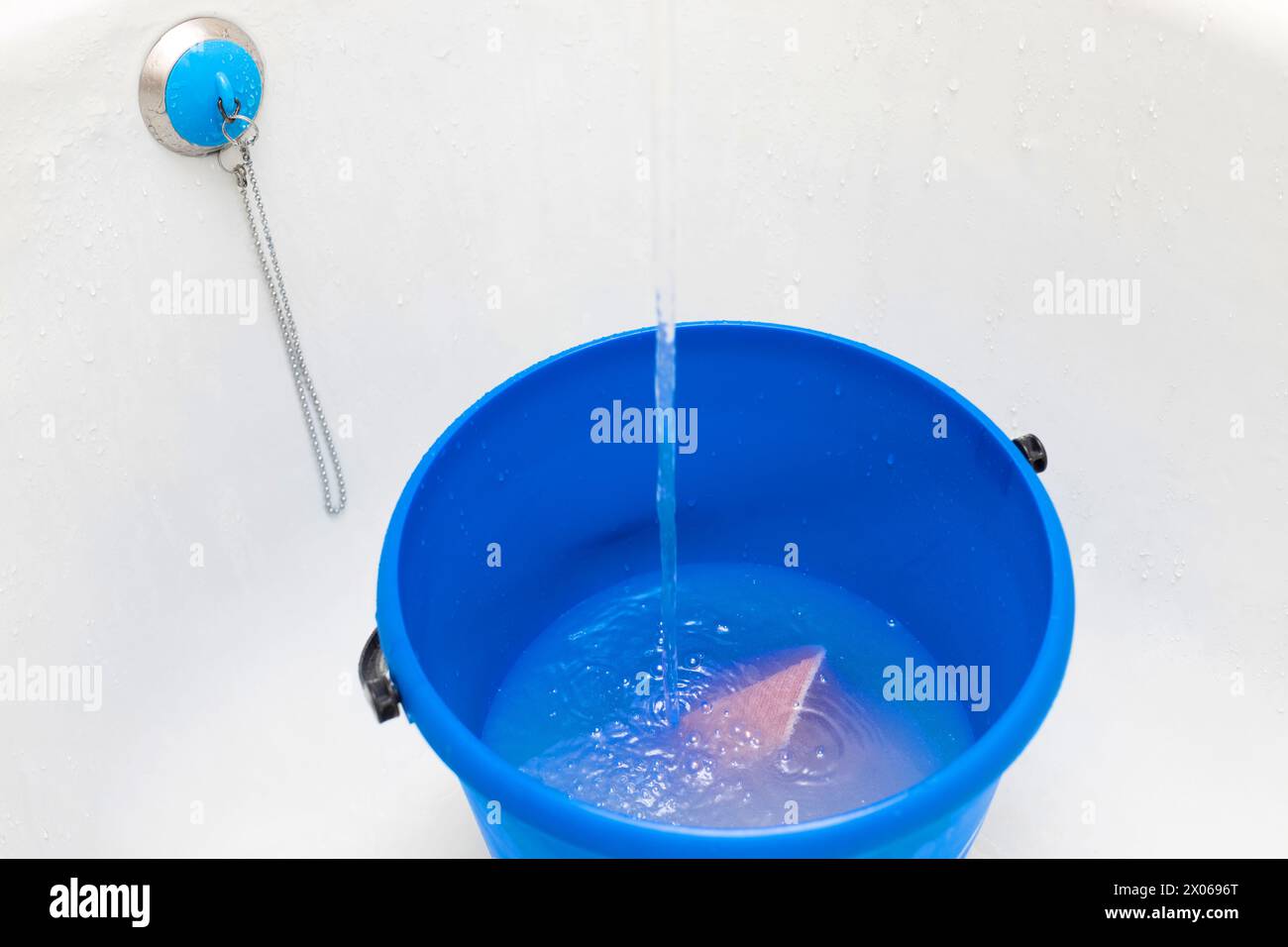 Wasser wird mit einem Lappen in einen Eimer gegossen. Füllen eines Eimers mit Wasser zur Reinigung. Blauer Kunststoffeimer mit Wasser Stockfoto