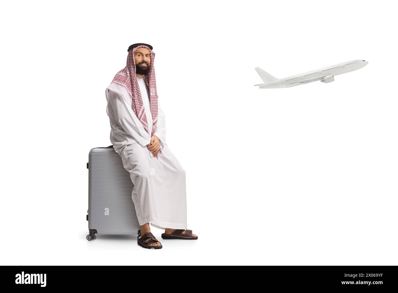 Saudischer arabischer Mann sitzt auf einem Koffer am Flughafen und ein Flugzeug, das isoliert auf weißem Hintergrund abhebt Stockfoto
