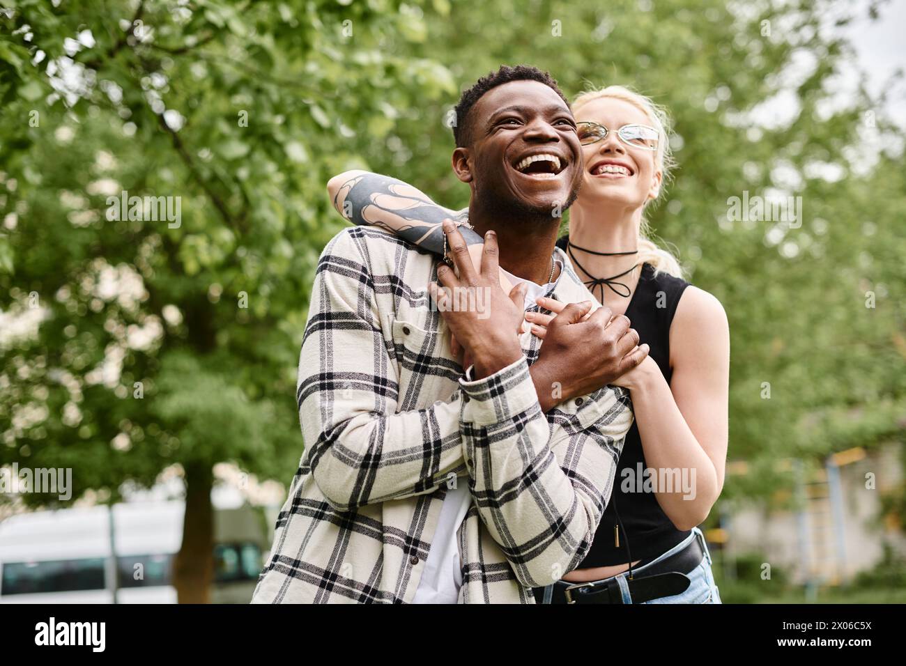 Ein glückliches multikulturelles Paar, ein Afroamerikaner, der draußen in einem Park eine kaukasische Frau in den Armen hält. Stockfoto
