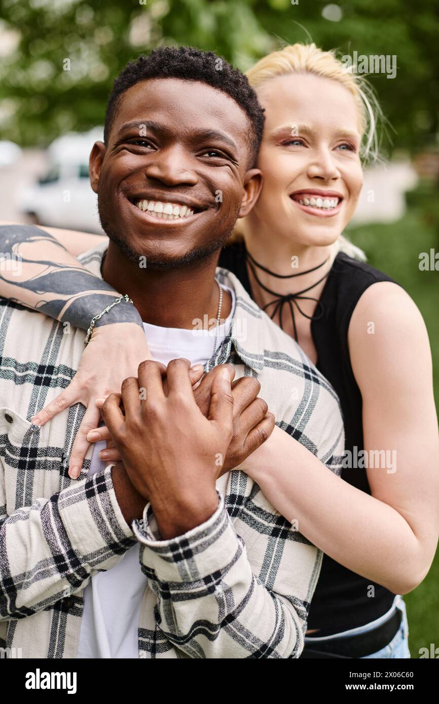Ein glückliches multikulturelles Paar - ein Afroamerikaner, der eine kaukasische Frau in den Armen hält - in einer romantischen Umarmung draußen in einem Park. Stockfoto