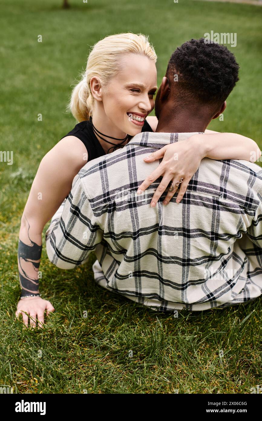 Ein glückliches multikulturelles Paar, ein Afroamerikaner und eine Kaukasierin, die sich eine zarte Umarmung auf dem Gras in einem Park teilen. Stockfoto