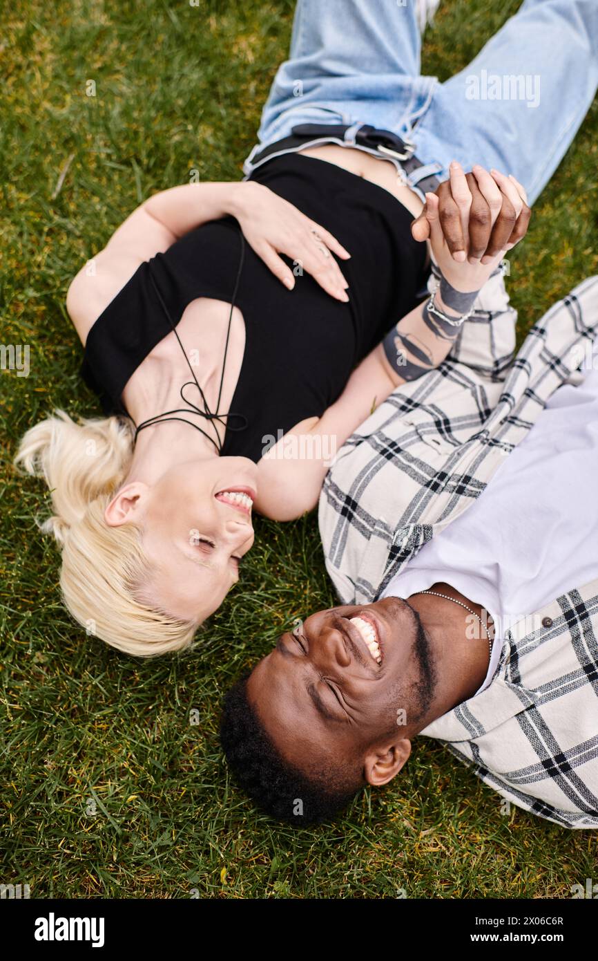 Ein glückliches, multikulturelles Paar, ein afroamerikanischer Mann und eine Kaukasierin, entspannen sich zusammen und genießen üppig grünes Gras in einem Park. Stockfoto