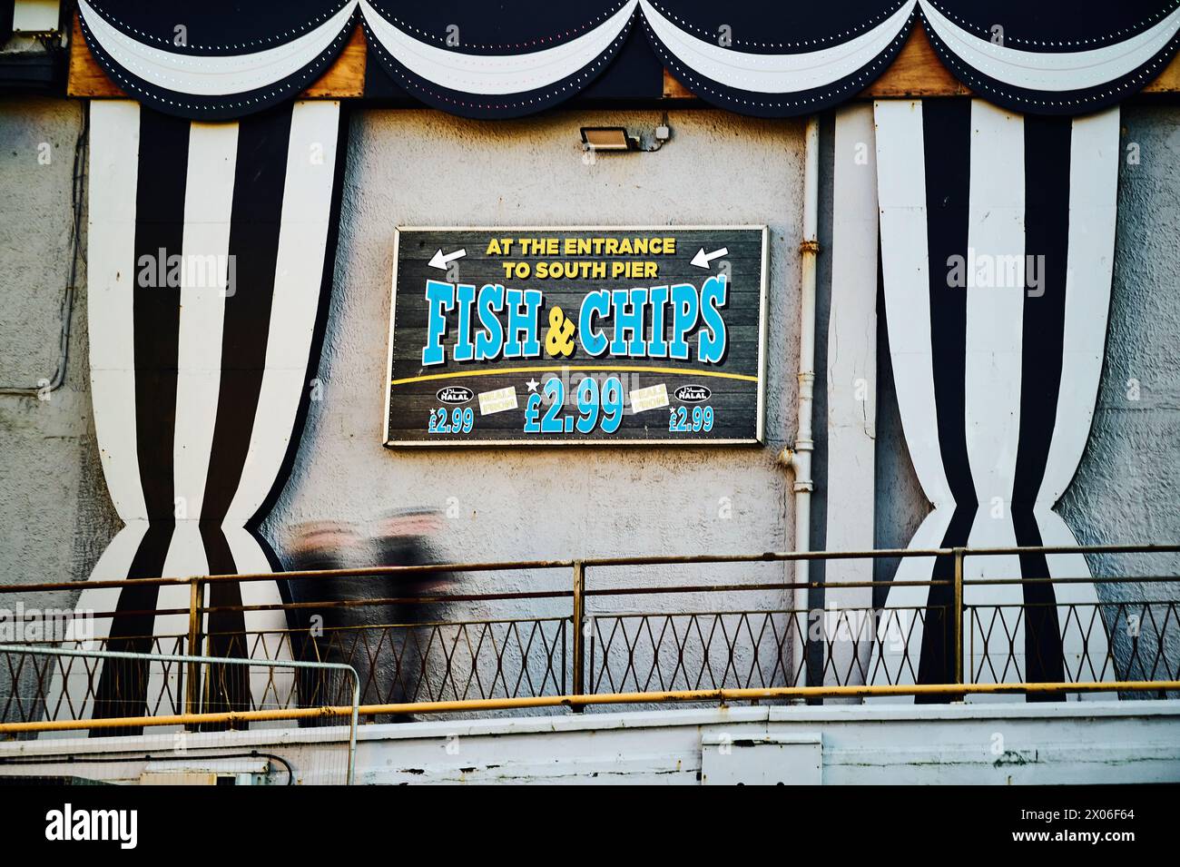 Ein Paar, das an einem Fish and Chips Schild am South Pier, Blackpool, Großbritannien vorbeiläuft Stockfoto