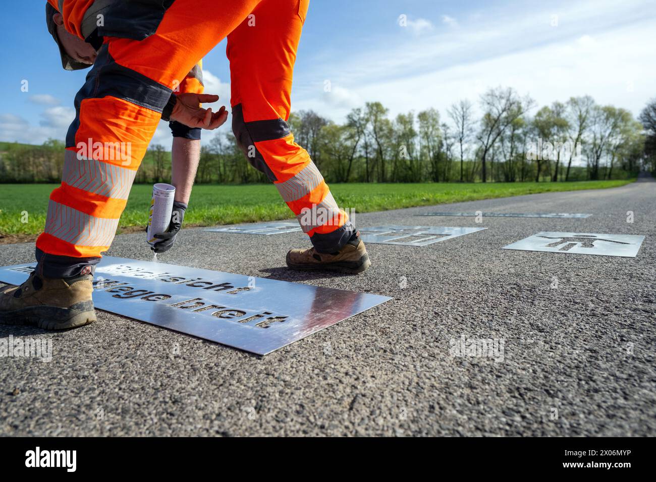 10. April 2024, Bayern, Stadtlauringen: Der Angestellte eines Bauhofs sprüht die Worte „Rücksicht macht Wege breit“ auf einem Feldweg. Andere Schablonen für Symbole eines Hundebesitzers, eines Traktorfahrers und eines Radfahrers liegen hinter ihm. Da Konflikte zwischen Landwirten, Wanderer, Radfahrern und Freizeitnutzern auf Land- und Forststraßen immer häufiger auftreten, fordert der Bayerische Bauernverband eine verstärkte Zusammenarbeit mit einer neuen Kampagne und Markierungen auf Feldwegen. Die ersten Logos wurden nun auf einem Weg bei Stadtlauringen im Landkreis Schweinfurt angebracht. Foto: Pia Bayer Stockfoto