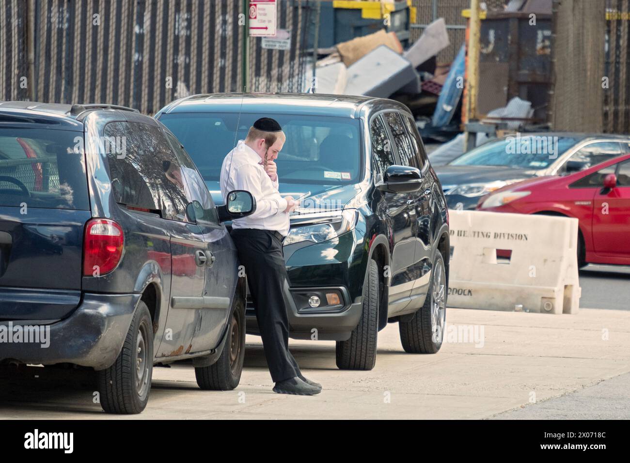 Ein chassidischer jüdischer junger Mann mit langem Peyot macht eine kurze Pause und liest von seinem Handy. In Brooklyn, New York. Stockfoto