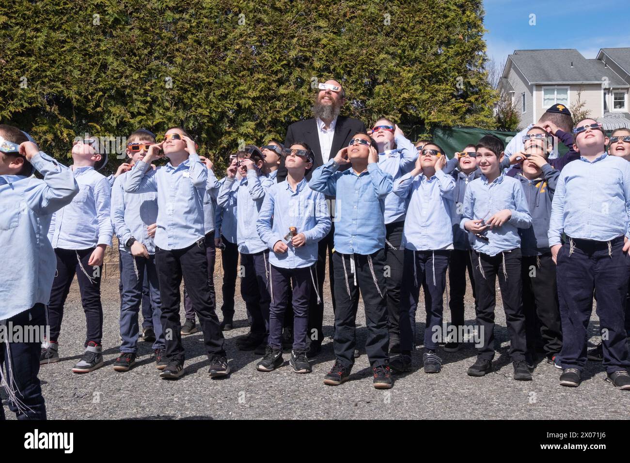 Ein orthodoxer Rabbiner und seine Schüler zur Zeit der Sonnenfinsternis 2024. Bis auf einen tragen alle eine Schutzbrille. Im Rockland County, NY. Stockfoto