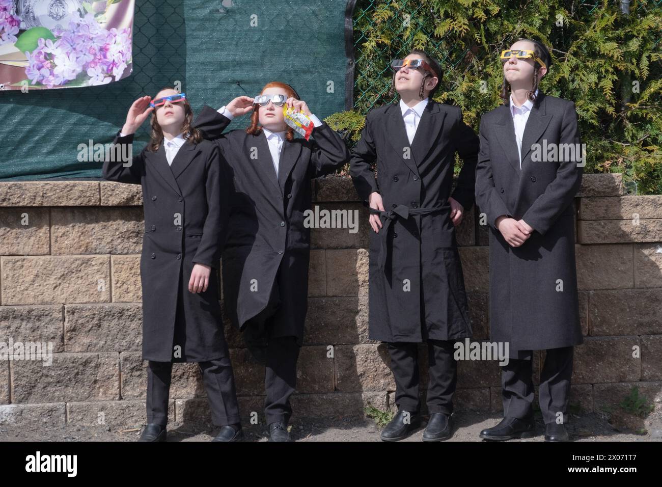 Auf ihrem Schulhof beobachten 4 orthodoxe jüdische Studenten die Sonnenfinsternis von 2024 durch eine Schutzbrille. Im Rockland County, New York. Stockfoto