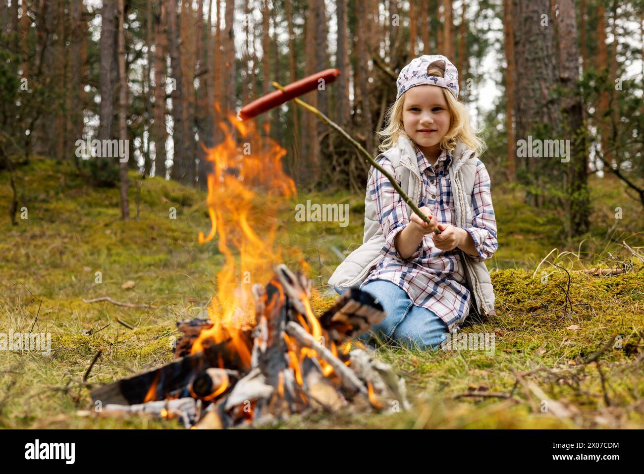 Kleines Mädchen, das Würstchen über Lagerfeuer im Wald brät. Outdoor-Abenteuer Stockfoto