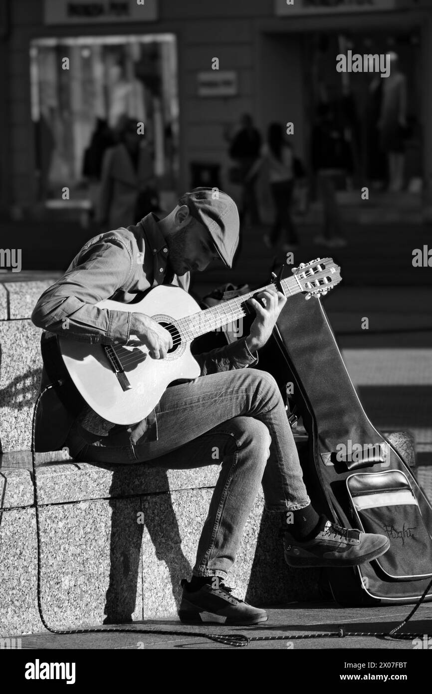 Gitarrist auf der Straße. Das Bild zeigt eine Person, die draußen Gitarre spielt, wahrscheinlich während einer Straßenaufführung. Stockfoto