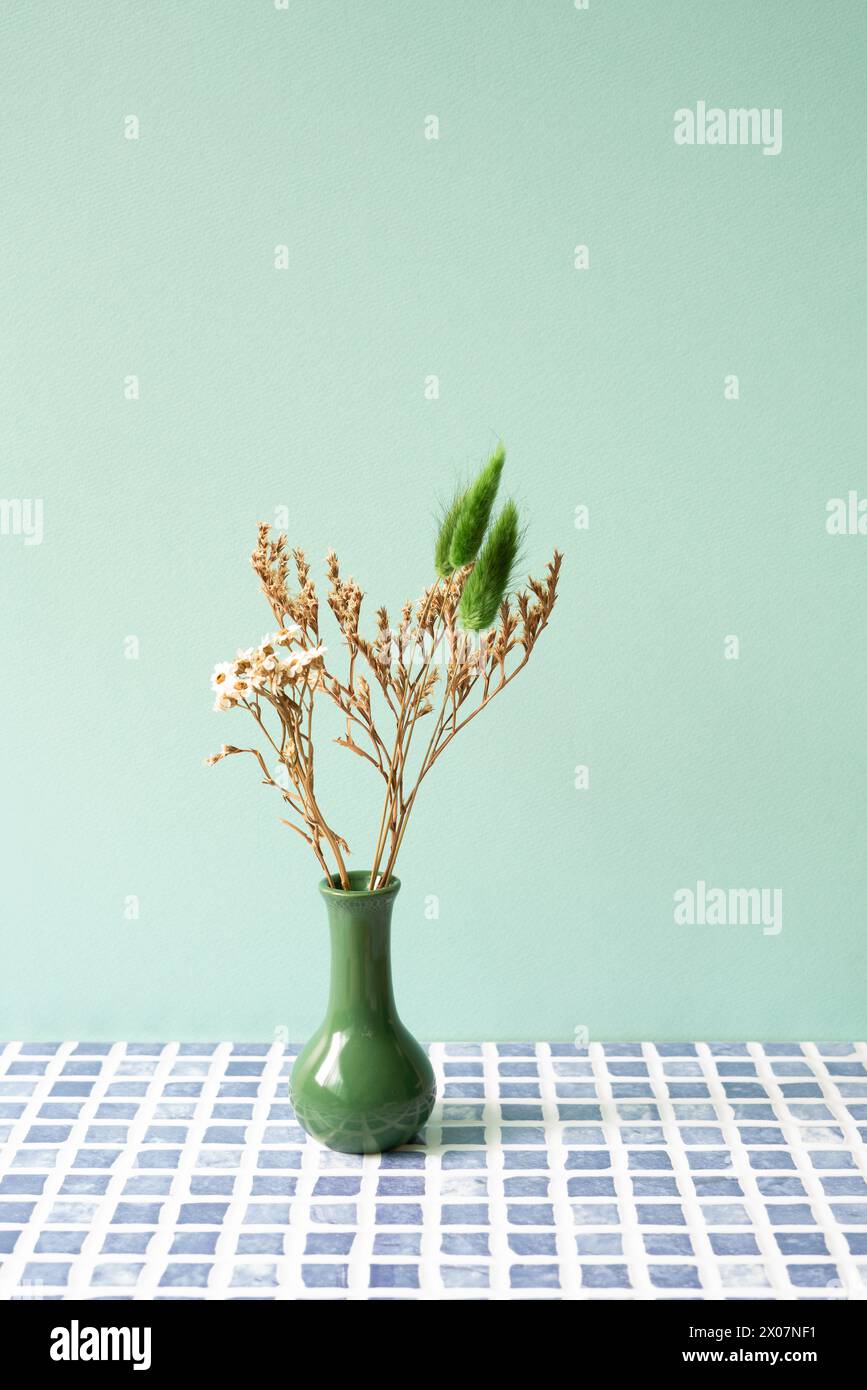 Grüne Vase mit trockener Blume auf blauem Fliesentisch. Mint. Wandhintergrund Stockfoto