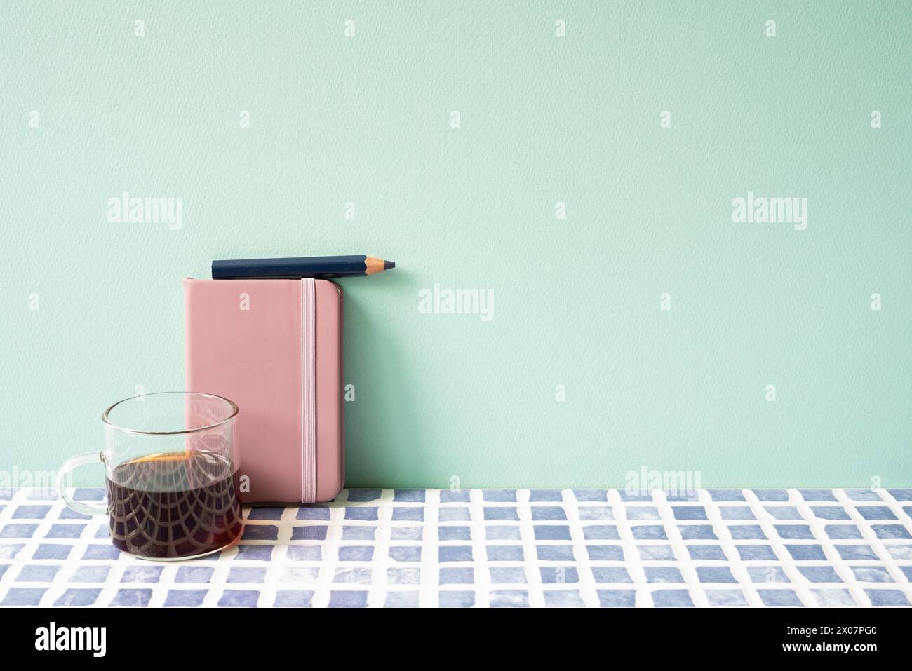 Tagebuch-Notizbuch, Bleistift, Kaffee auf blau gefliestem Schreibtisch. Mint. Wandhintergrund. Arbeitsbereich Stockfoto