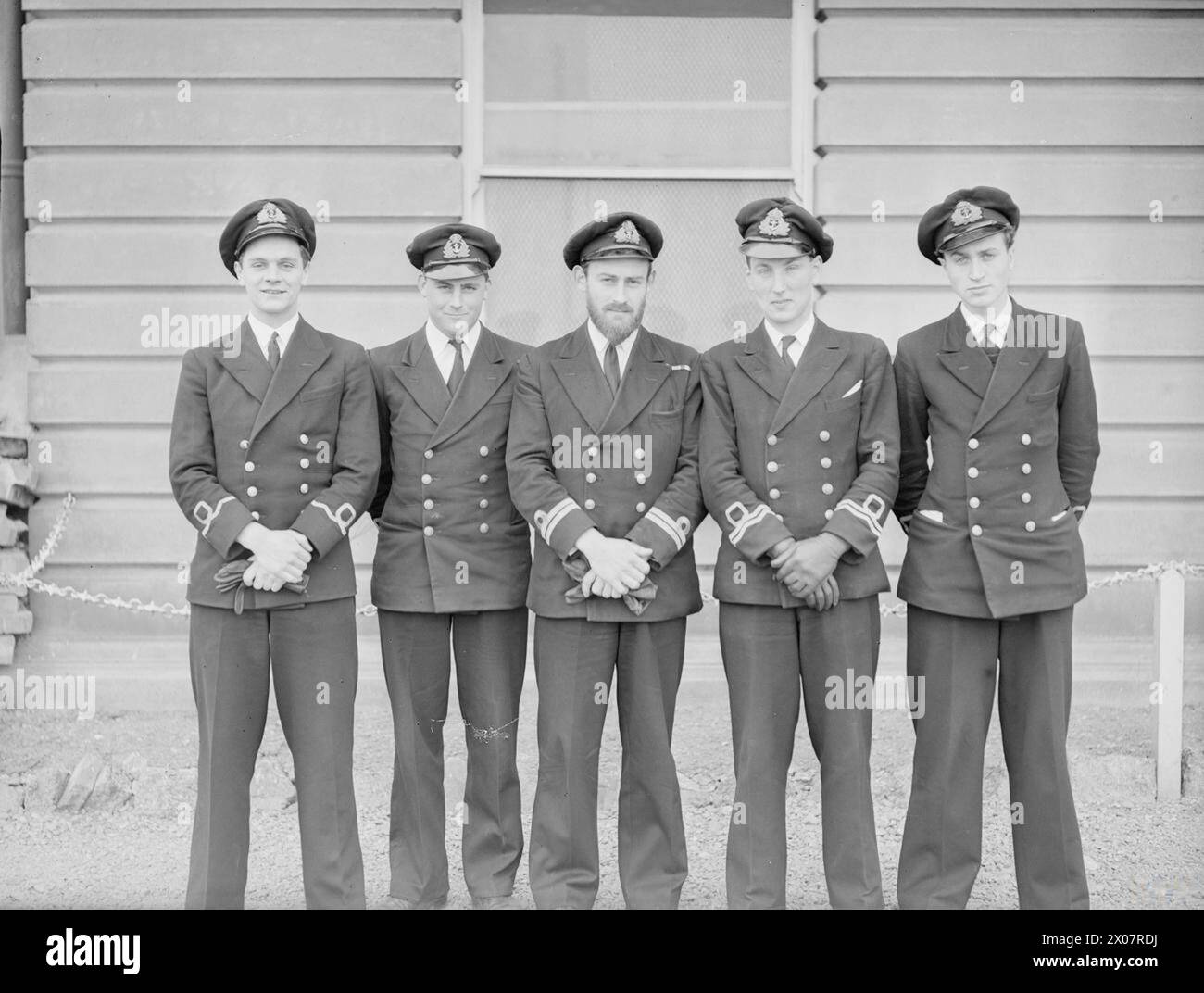 DICKENS URENKEL FÜHRT ANGRIFF AUF FEINDLICHE BEWAFFNETE TRAWLER AN. LIEUT PETER G C DICKENS, DSC, MBE, RN, URENKEL DES BERÜHMTEN SCHRIFTSTELLERS, MIT SEINEN OFFIZIEREN, NACHDEM LEICHTE KÜSTENKRÄFTE UNTER SEINEM KOMMANDO ZURÜCKGEKEHRT WAREN, NACHDEM SIE DREI FEINDLICHE BEWAFFNETE SCHLEPPNETZFISCHER VOR DER NIEDERLÄNDISCHEN KÜSTE ERFOLGREICH ANGEGRIFFEN HATTEN, WURDE EINER VERSENKT. - Von links nach rechts: Sub Lieut David Moore, RNZNVR, Sub Lieut George James MacDonald, DSC, RNZNVR, Lieut Peter G C Dickens, MBE, RN (SO), Lieut A C Jensen RNVR und Sub Lieut Gordon Noel Fish, RNVR Stockfoto