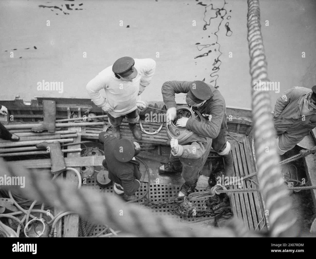 1941 wurde ein Taucher an Bord der HMS Suffolk in einem Taucheranzug vorbereitet, um die Propeller des Schiffes nach der Navigation auf einem Eisfeld auf Schäden zu untersuchen. Stockfoto
