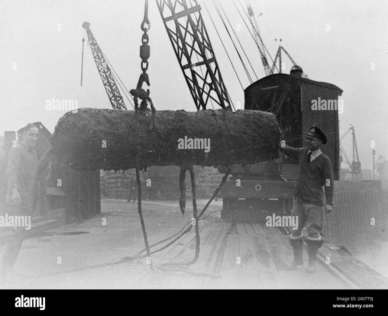 MARINEBOMBENEXPERTEN. 6. OKTOBER 1941, RODING RIVER, BELLING CREEK. ZWISCHEN DEN GEZEITEN ARBEITETE LIEUTENANT COMMANDER JOHN BRYAN PETER MILLER, GC, RNVR, ZUSAMMEN MIT DEM FÄHIGEN SEEMANN STEPHEN JOHN TUCKWELL, GC, EINE MINE AUF DEM MATSCHIGEN BODEN DES RODING RIVER, DER IN DEN BELLING CREEK MÜNDET, SICHER. ZWISCHEN IHNEN MACHTEN SIE DIE BOMBE UNSCHÄDLICH UND LIESSEN SIE SPÄTER MIT EINEM KRAN VOM EINGANG ZU EINER KANALISATION ENTFERNEN, IN DER SIE RUHTE. - Auf der rechten Seite ist Lieut Cdr John Bryan Peter Miller, GC, RNVR, (dann Lieut) und links, Able Seaman John Tuckwell, GC, mit der riesigen Bombe, die sie sicher gemacht und aus dem Roding River gezogen hatten Stockfoto