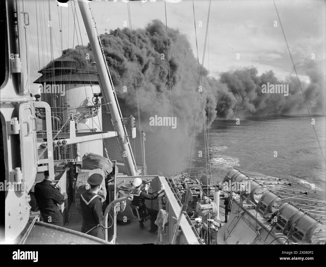 Die HMS Mauritius legt einen dichten Rauchschirm auf dem Meer, der von der Brücke des Kreuzers aus beobachtet wird, mit Radargeräten, die während des Zweiten Weltkriegs teilweise sichtbar sind Stockfoto