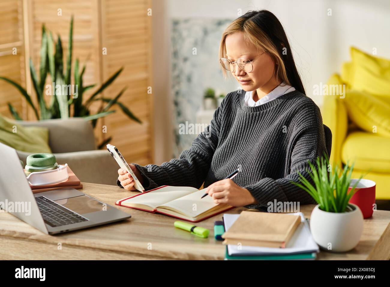 Ein junges asiatisches Mädchen, das am Schreibtisch sitzt und sich während des Studiums zuhause auf einen Laptop und ein Notebook konzentriert. Stockfoto