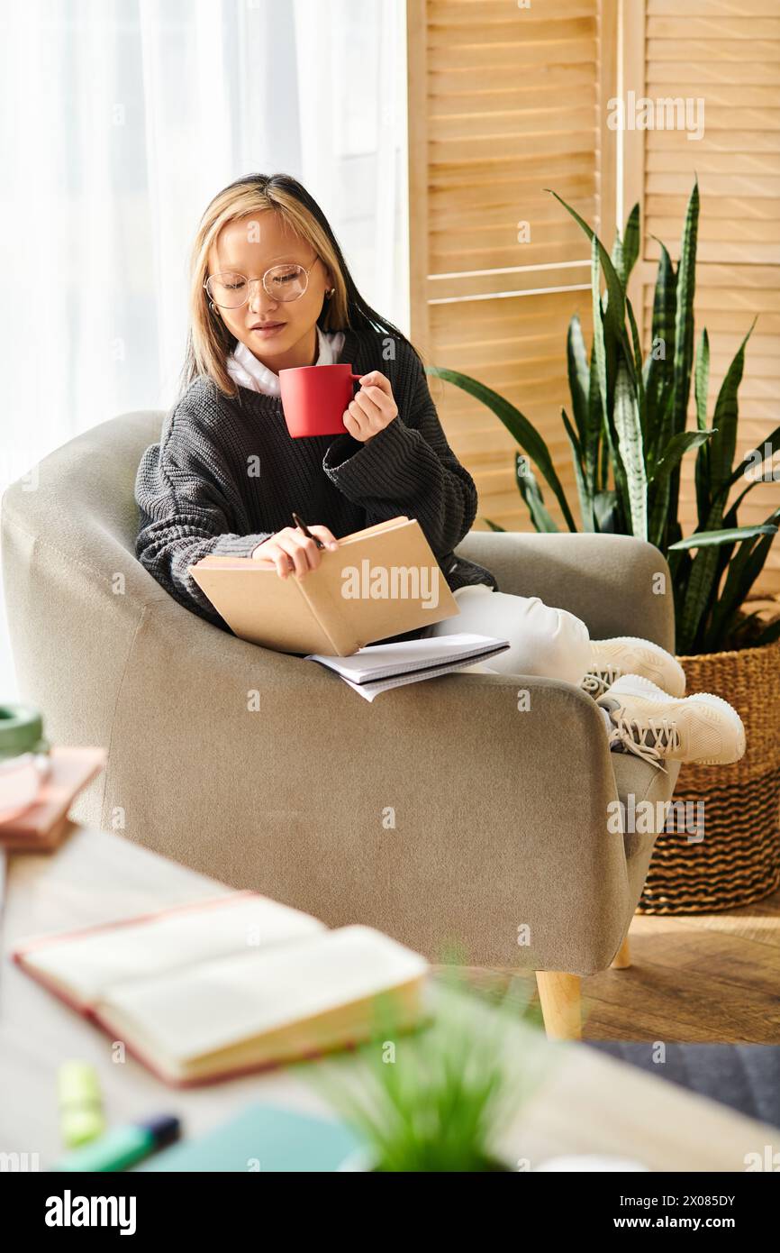 Eine junge asiatische Frau sitzt auf einem Stuhl, tief besinnend und hält sanft eine Tasse Kaffee in der Hand. Stockfoto