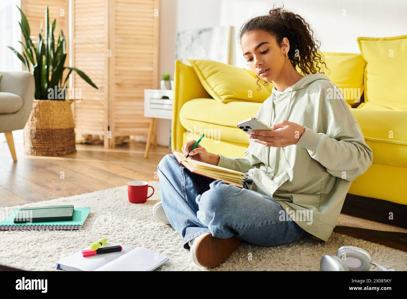 Eine junge Frau mit Notizbuch und Stift sitzt auf dem Boden, in Gedanken gesogen, umgeben von den Werkzeugen der Inspiration. Stockfoto