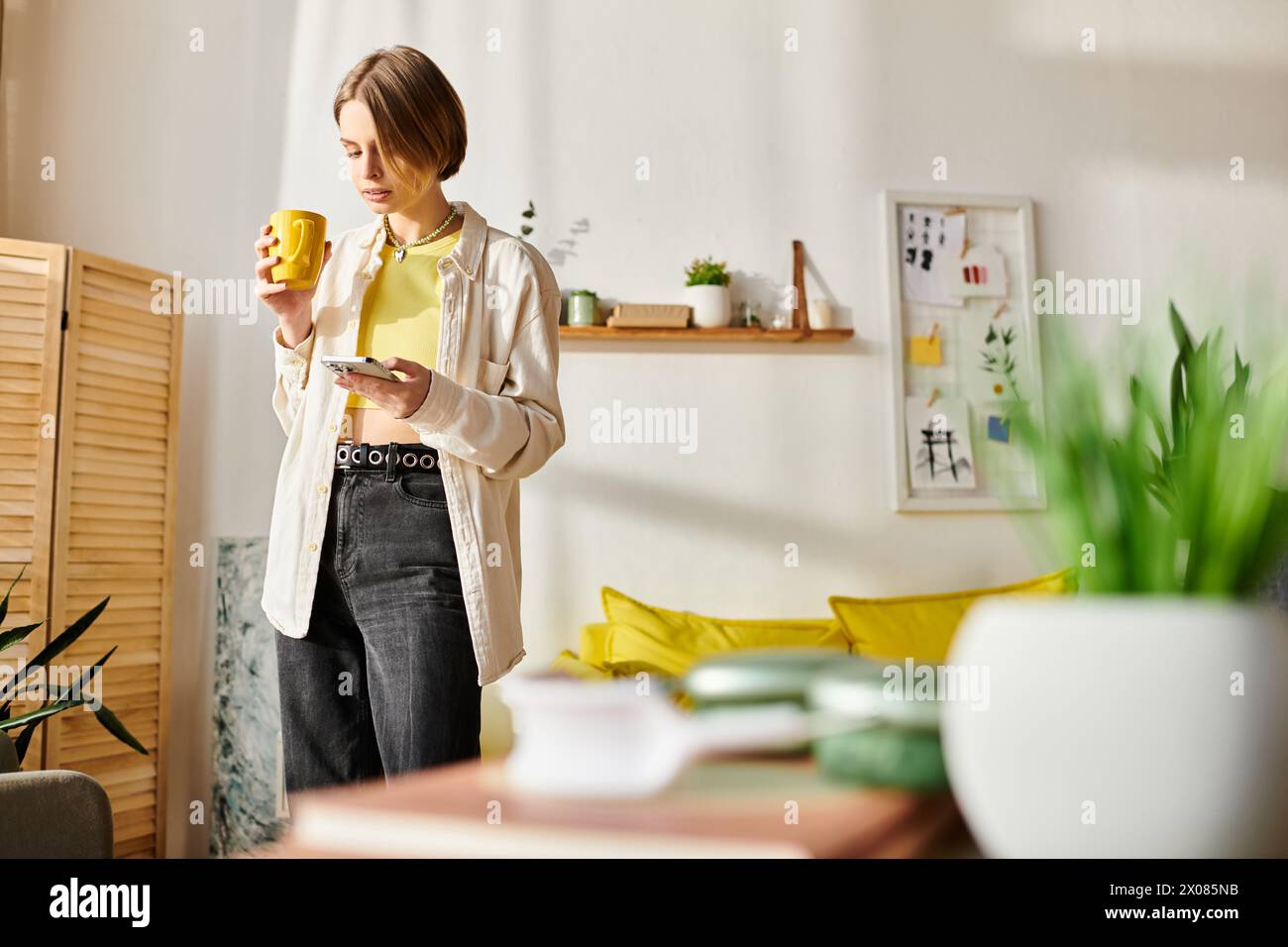 Ein heiterer Moment, als ein Teenager in ihrem gemütlichen Wohnzimmer steht und während ihrer E-Learning-Session eine Tasse Kaffee genießt. Stockfoto